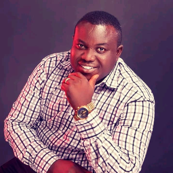 Smiling man in checkered shirt rests his chin on his hand wearing a gold watch.