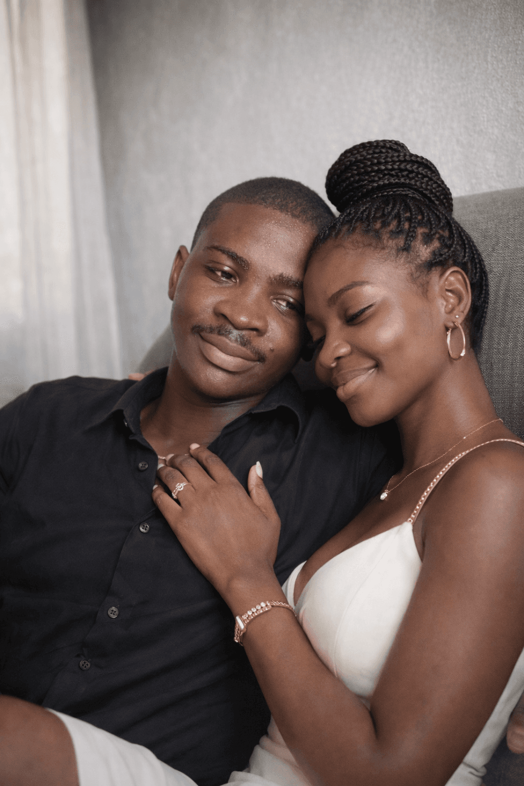 Engaged Black couple embracing, woman smiling with eyes closed, man looking ahead.