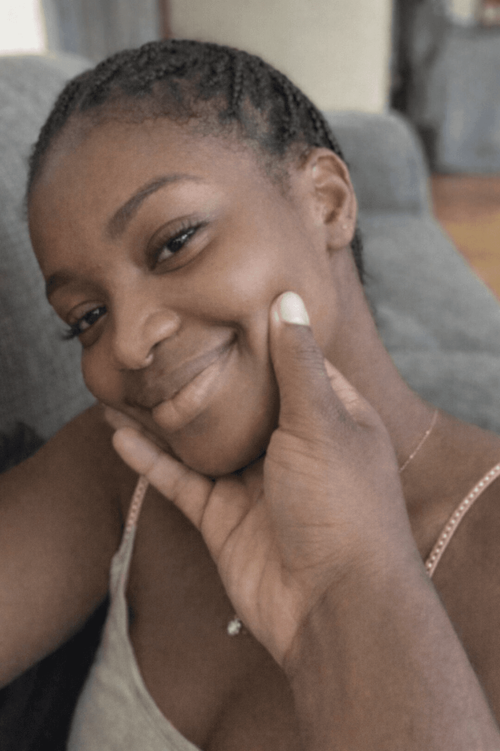 Young Black woman with braided hair smiles as a hand gently cradles her face.